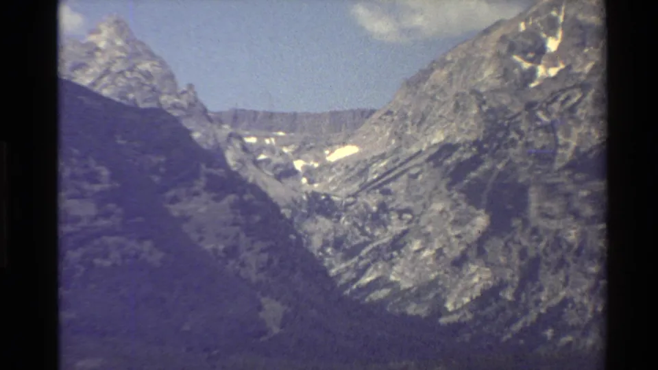Closer 1980 Western USA 8mm view into a rugged mountain valley, with pale snow remnants and textured rocky faces.