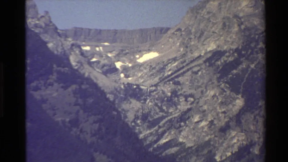 1980 Western USA 8mm frame near the end of the zoom, showing a rocky peak, valley wall, snow patches, and faded color.