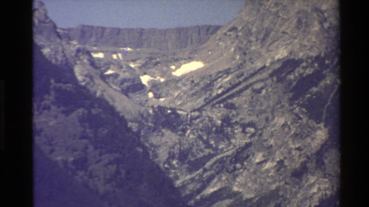 Rocky mountain valley with patches of snow under a bright sky.