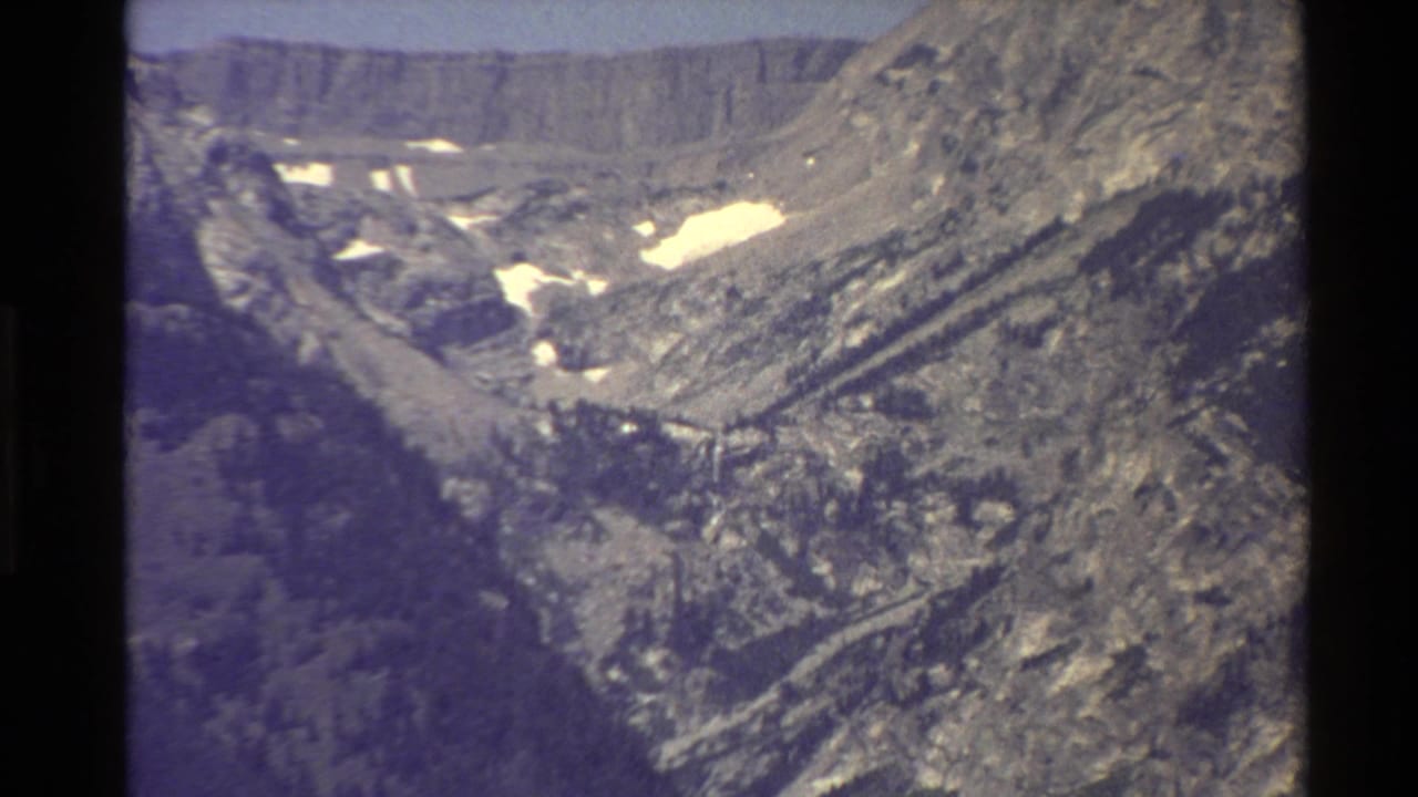 Mountain slope and valley with scattered snow patches and dark shadows.