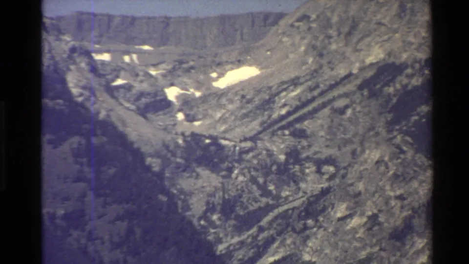 1980 Western United States home-movie frame showing a sunlit rocky valley, melting snow patches, and a high ridgeline in soft 8mm color.