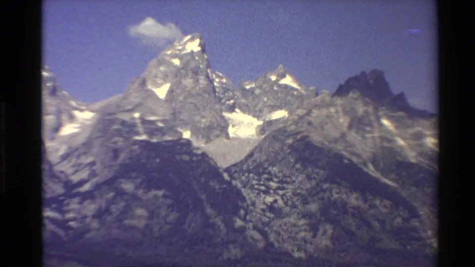 Closer 8mm view of Western U.S. mountain peaks with bright snowfields, rugged rock faces, and soft handheld framing.