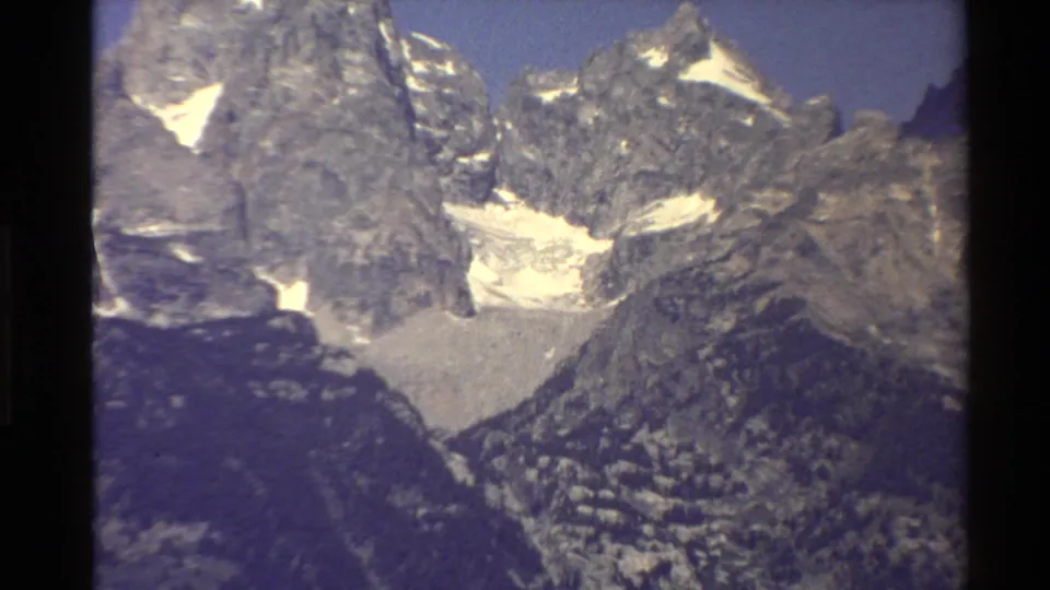 Close Western U.S. mountain frame showing steep rocky faces, white snowfields, shadowed lower slopes, and vintage 8mm softness.