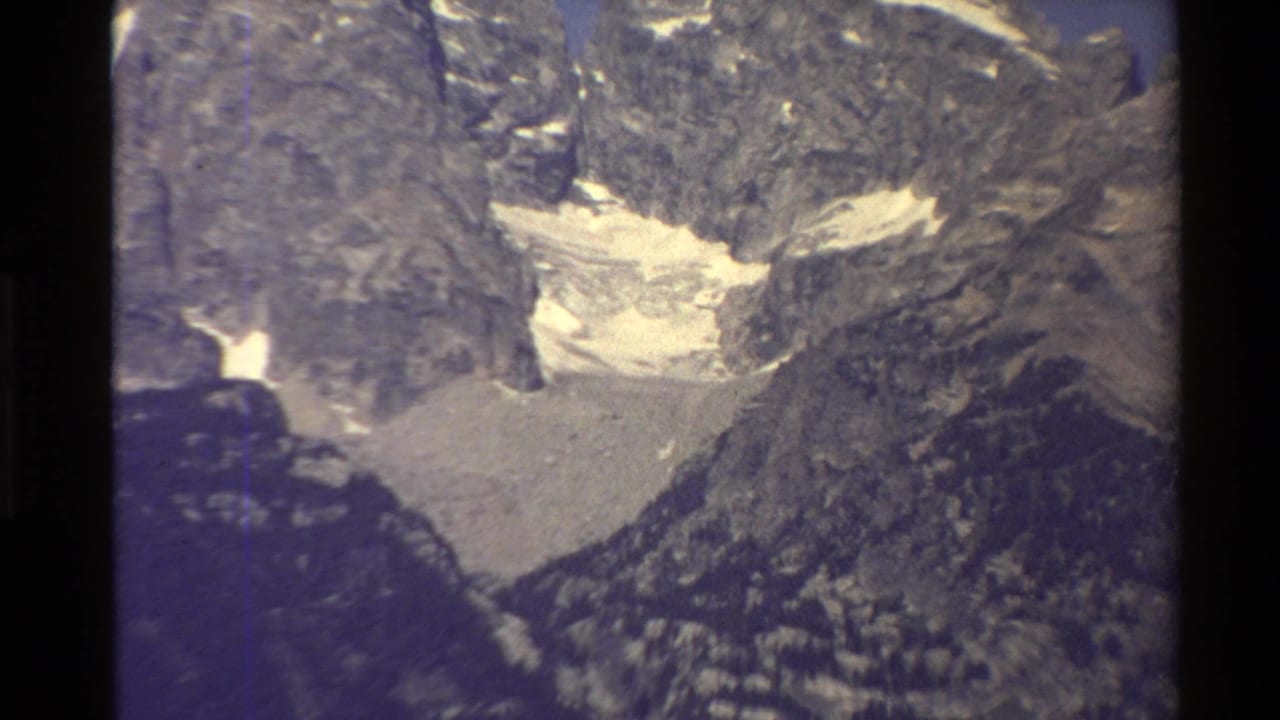 1980 Western U.S. home-movie frame showing a distant rocky basin with pale glacier or snow below dark mountain walls.