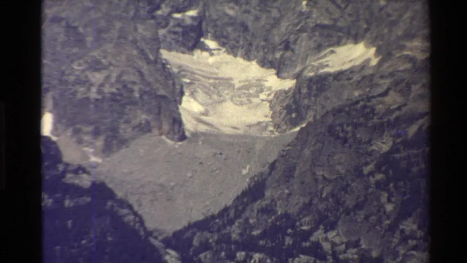 Western U.S. archival home-movie still of pale alpine ice or snow set between steep rocky slopes.