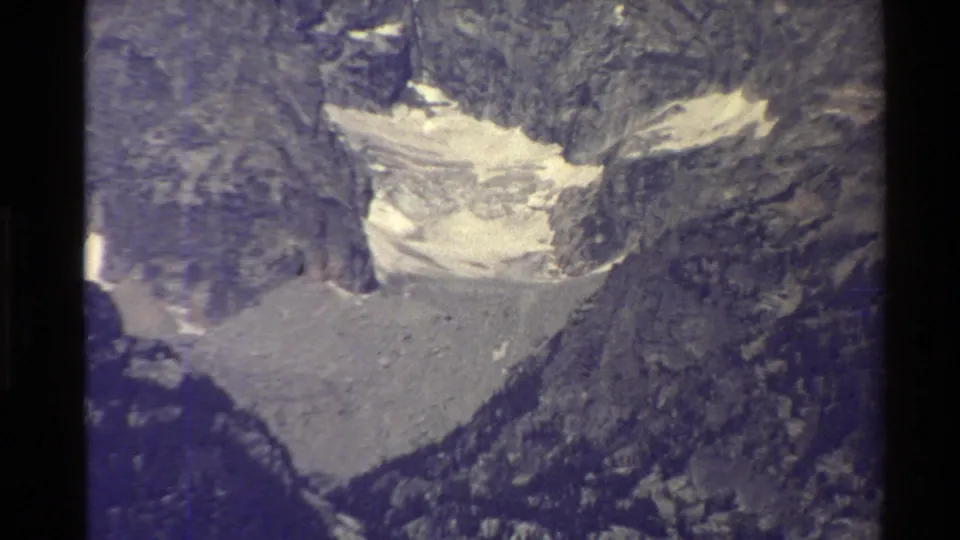 Soft, grainy 1980 home-movie view of a rugged alpine basin with pale snow or glacier material below rocky walls.