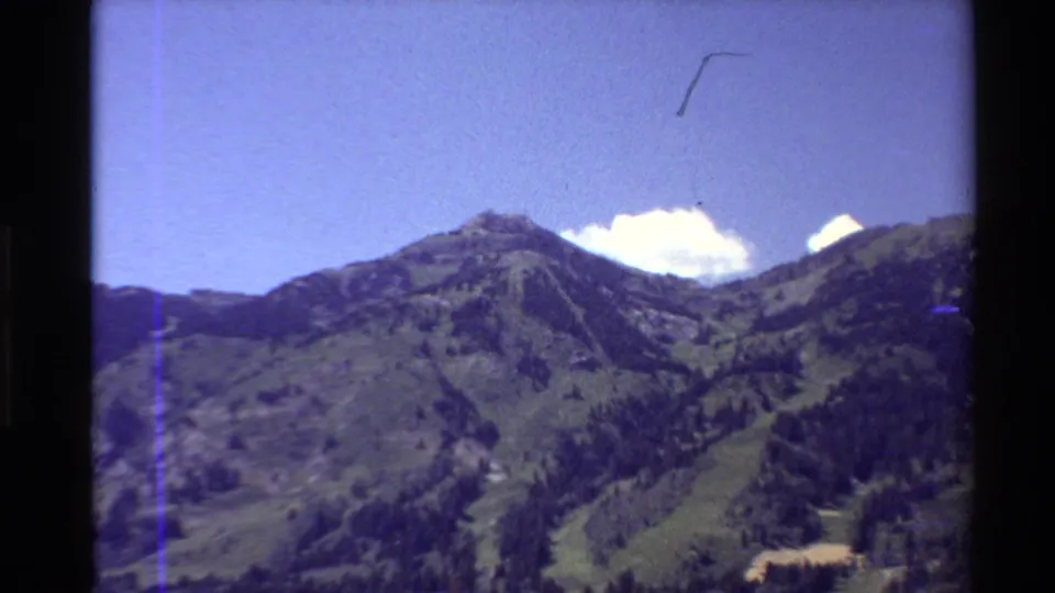 Final 8mm frame of a summer mountain ridge and dry ski-area slopes, with blue sky and visible film wear.
