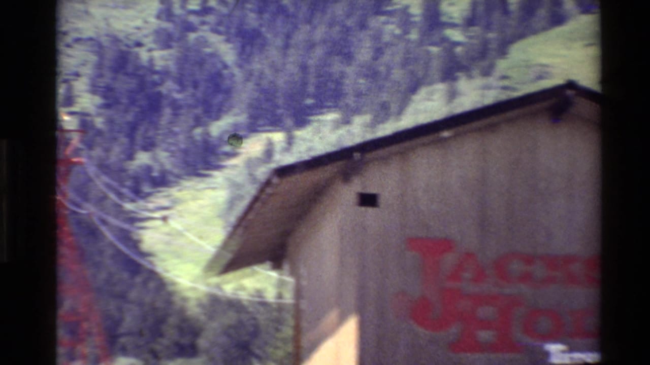 1980 Western USA home-movie frame showing a wooden building with red Jackson Hole Teton Village lettering and trees behind it.