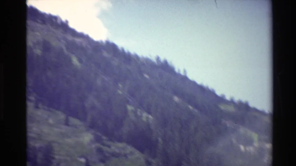 1980 Western USA mountain slope with forested ridge, open green terrain, and pale sky in handheld 8mm footage.