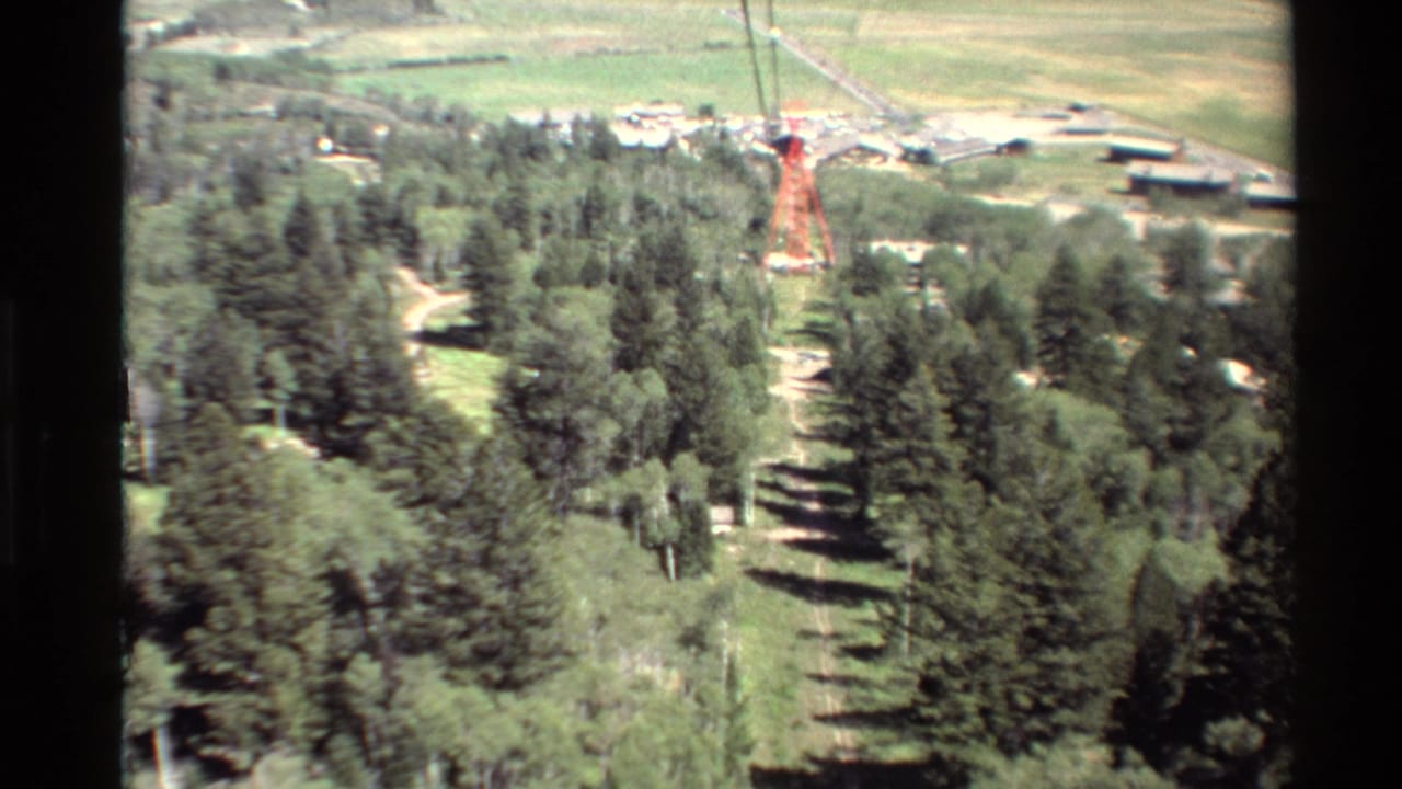 1980 Western U.S. home-movie frame looking from an elevated position across trees, fields, and a red tower structure.