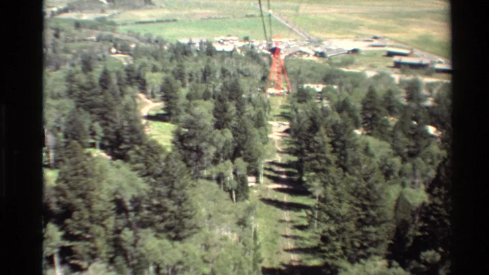 1980 Western U.S. home-movie frame looking from an elevated position across trees, fields, and a red tower structure.