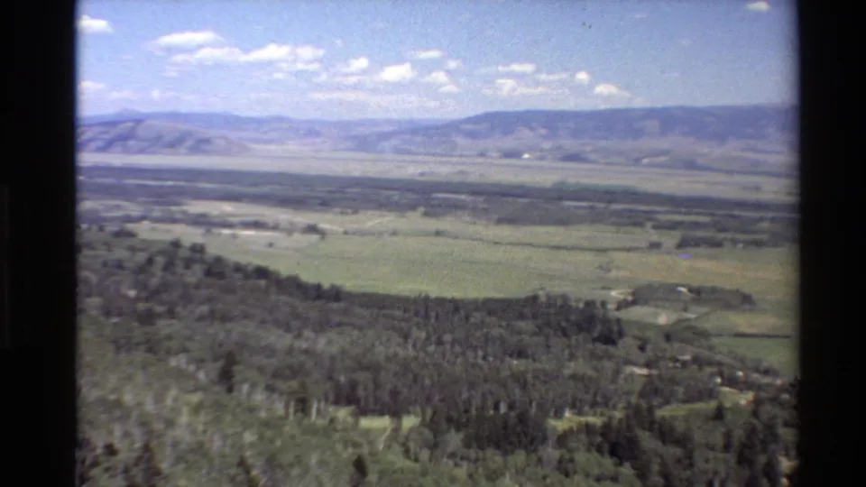 1980 Western U.S. home-movie frame showing a wide rural valley from an elevated moving viewpoint.