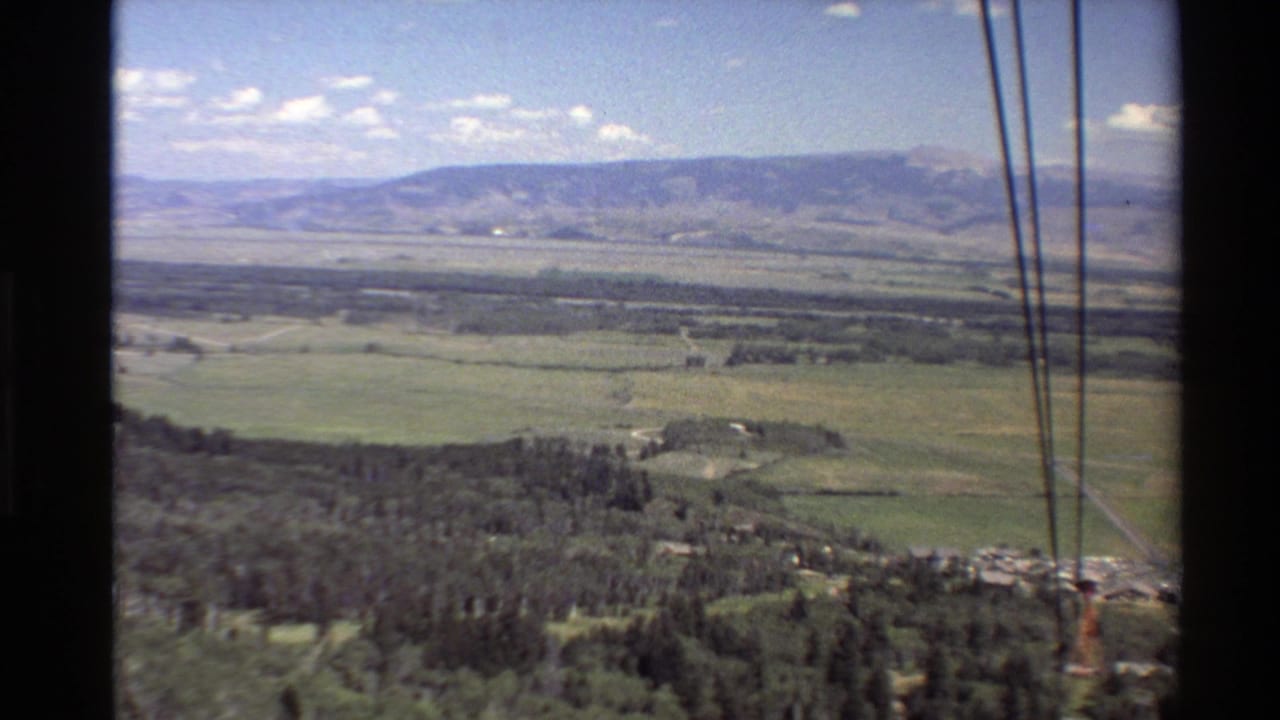 A Western USA valley stretches toward distant mountains while thin gondola or lift cables cross the right side of the 8mm frame.