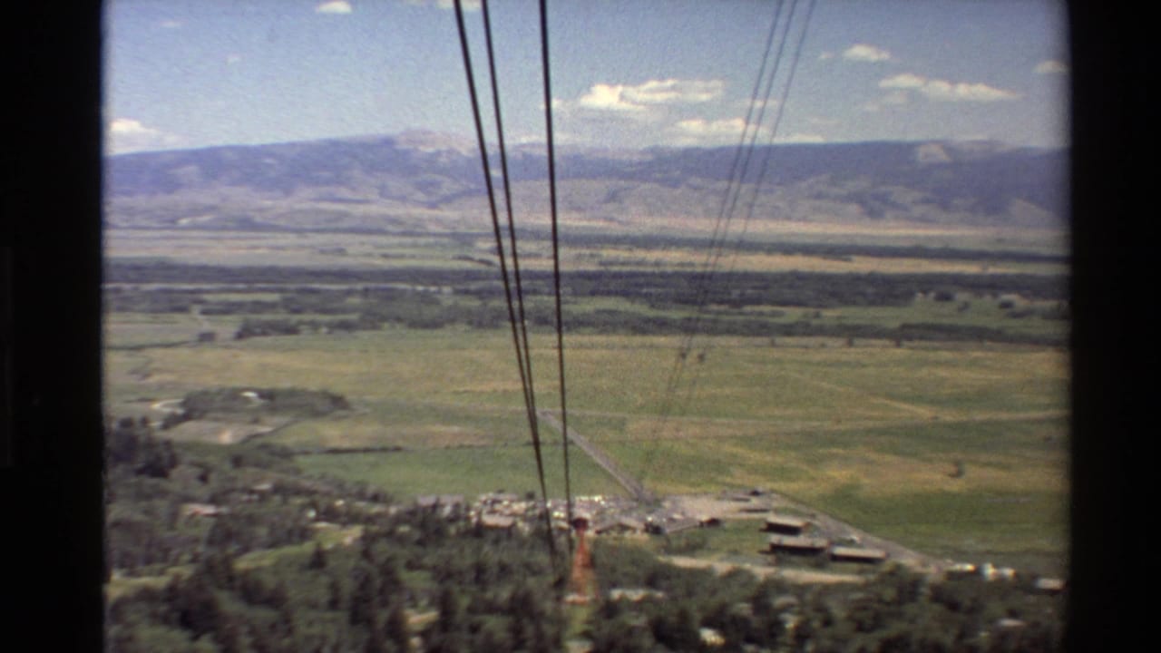 1980s 8mm Western U.S. cable car view looking over pasture, trees, small structures, and distant mountain ranges.