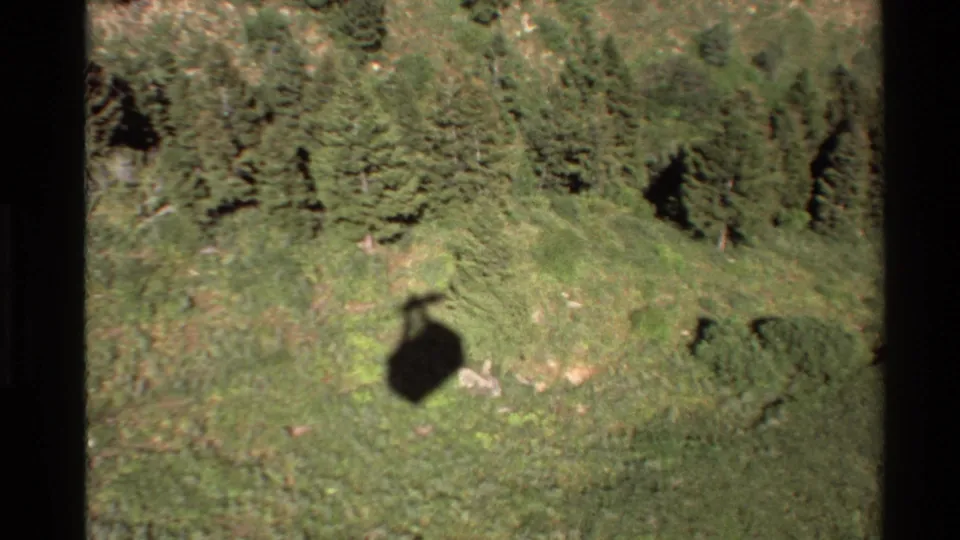 Aerial 8mm view in the Western USA showing the aircraft shadow moving across meadow and evergreen forest.