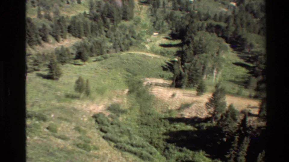 Western USA 1980 home-movie aerial view of forested mountain landscape, open meadow, and sloping terrain.