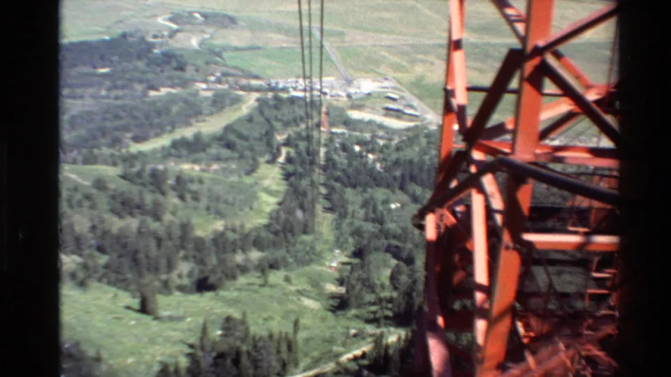 An orange steel support tower fills the right foreground as the tram route passes over a forested Western USA valley.