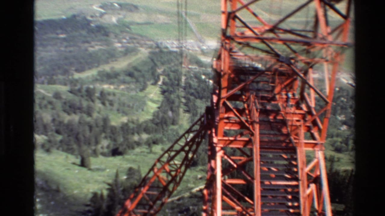 1980 Western U.S. 8mm view of a red cable support tower passing close to the camera above green forested hills and distant plains.