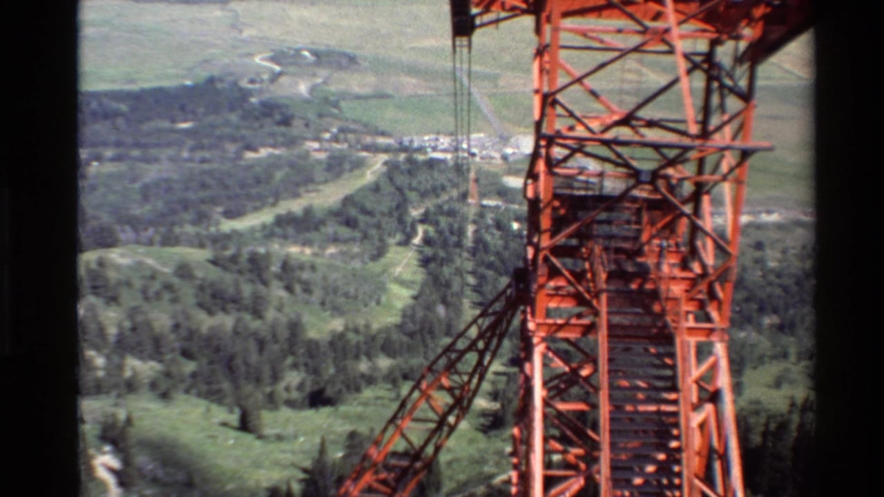 Red cable tower and suspended lines over green hills with plains in the distance.