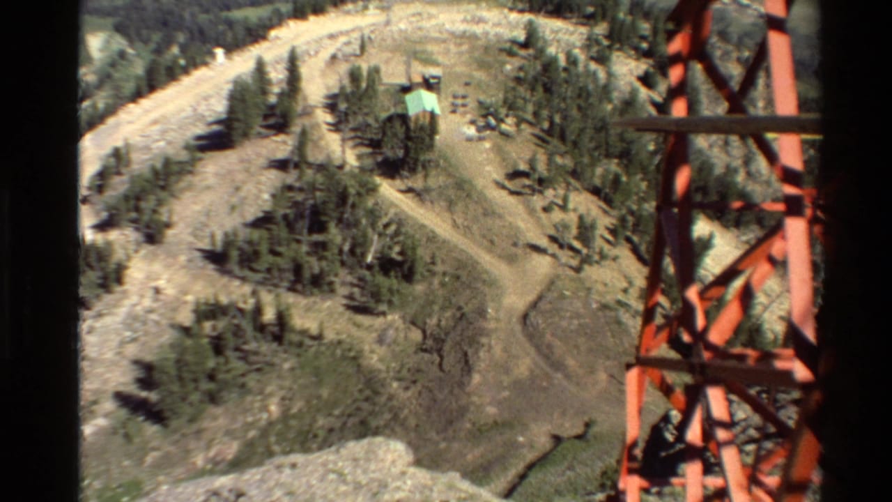 Mountain ridge with a red tower at right, dirt roads, trees, and a small green-roofed structure.