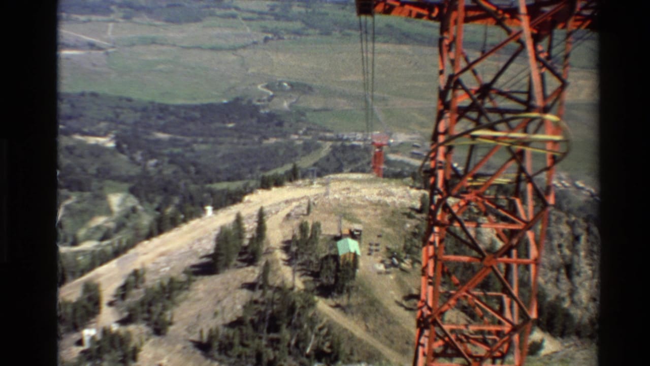 1980s 8mm view of a red electrical transmission tower on a Western U.S. mountain ridge with valleys and evergreens below.
