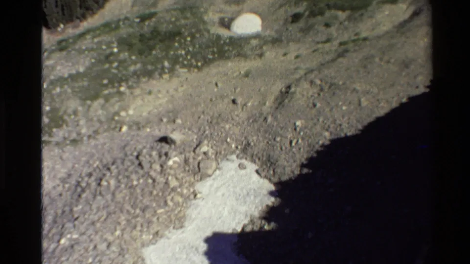 Close 8mm view of a rocky mountain slope with pale exposed ground and shadow cutting across the frame.