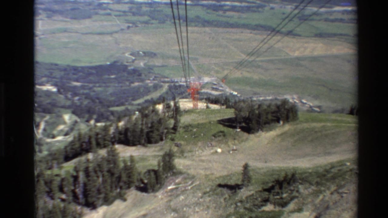 1980 Western USA 8mm frame looking over cable lines, a wooded hilltop, rocky slope, and distant valley fields.