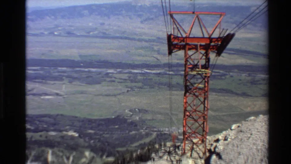 1980 Western USA 8mm view of a red cable car tower on a rocky hilltop, with cables leading across a broad valley.