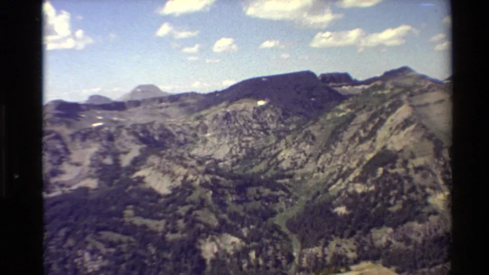 Western USA archival 8mm frame showing a panoramic mountain landscape with dark ridges, rocky slopes, valley contours, and clouds.