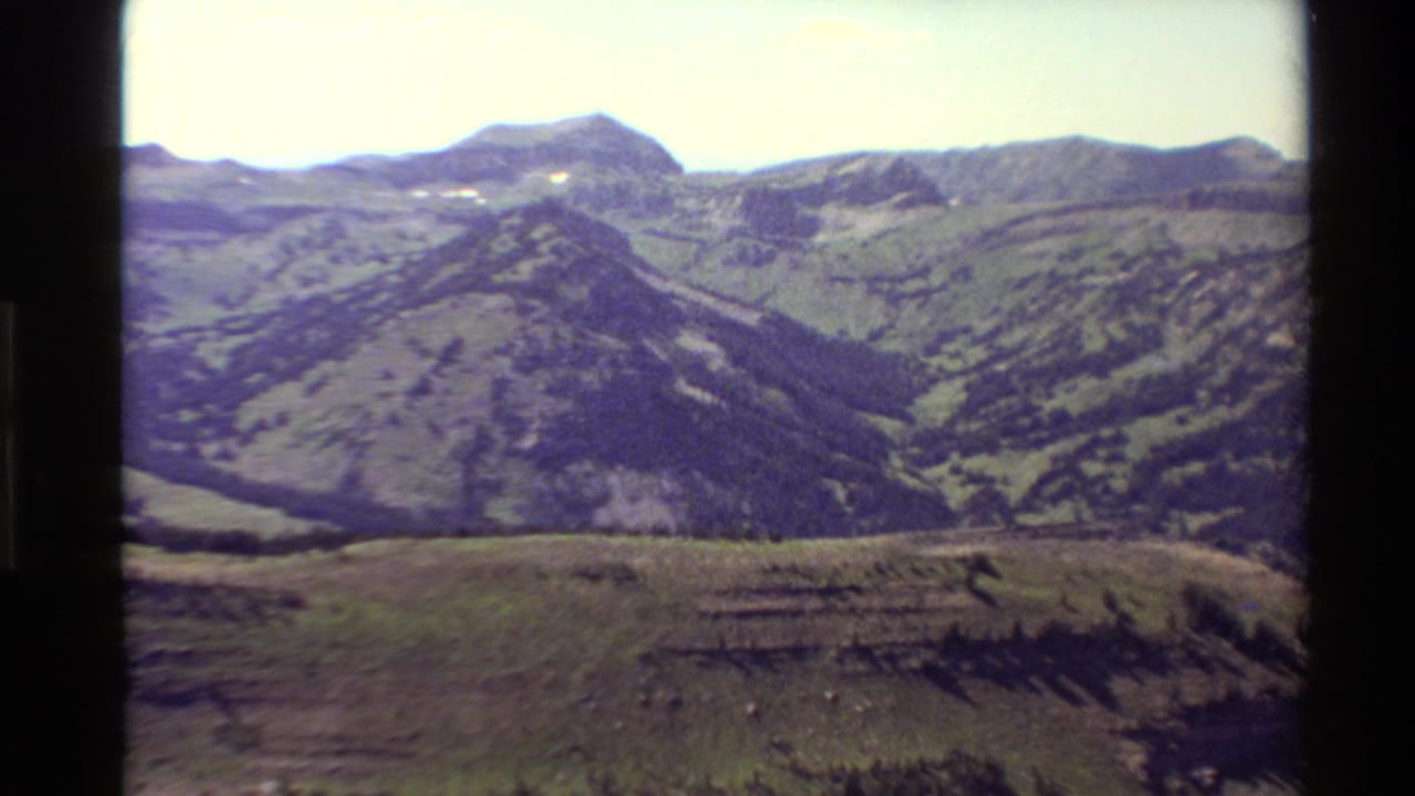 Western USA mountain panorama on 8mm film, with rolling green and purple-toned hills and no visible people or structures.