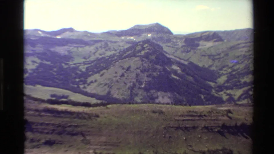 Archival 1980 8mm view of a mountain ridge, foreground hillside, valley shadows, and faded color typical of home-movie film.