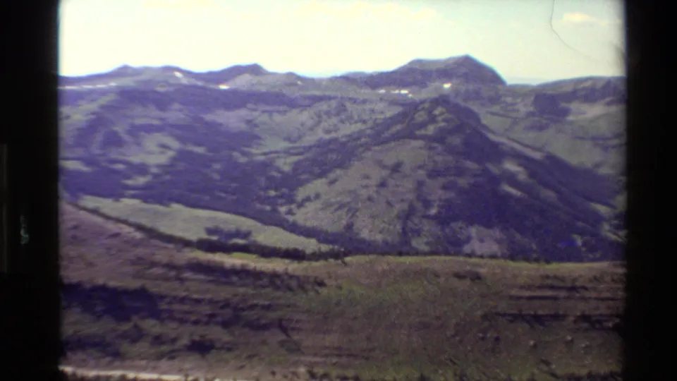 Final 8mm frame of the Western USA panorama, showing broad mountain ridges, sparse tree cover, and a pale sky with home-movie softness.