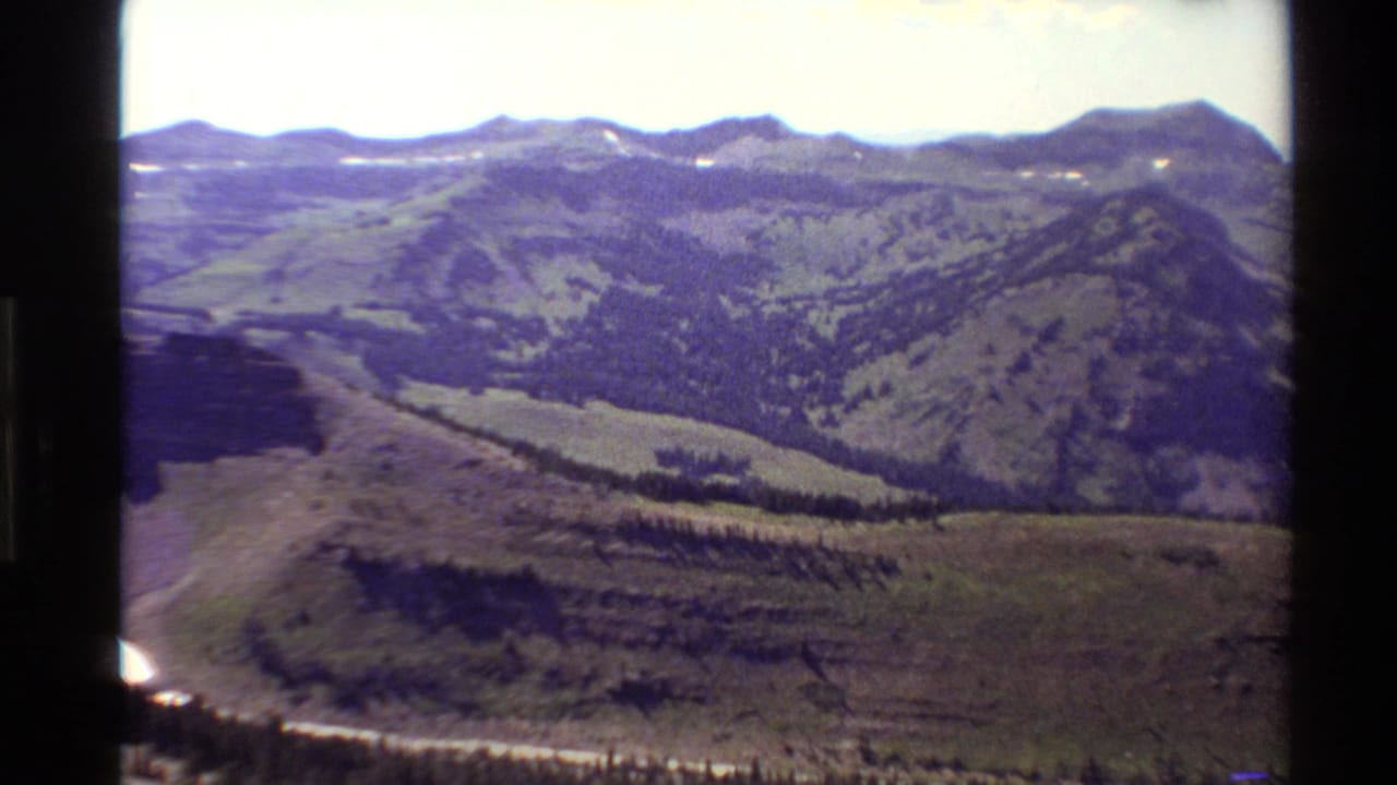 1980 Western USA home-movie view of a winding dirt road below forested mountain slopes and distant ridges.