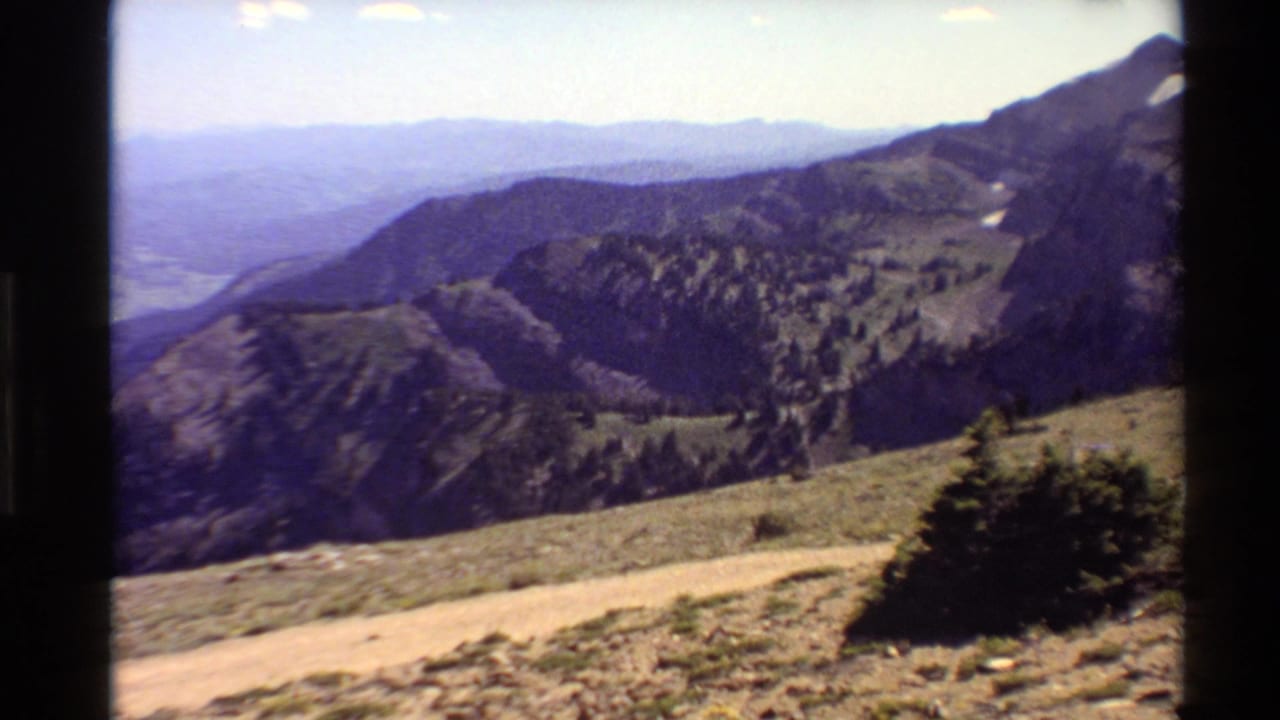 Mountain ridges seen from a high overlook with a dirt path and rocky foreground.