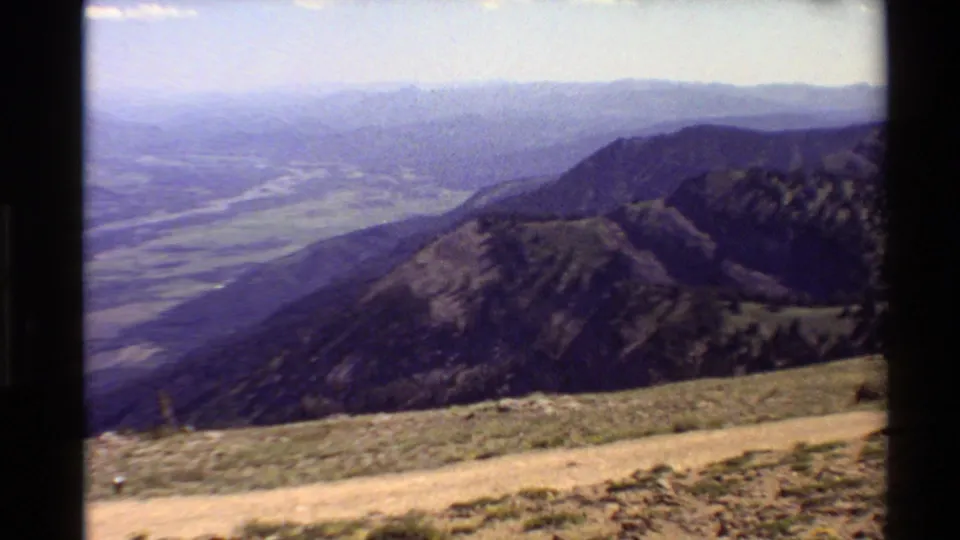1980 Western USA frame showing a hazy valley, layered mountains, a foreground dirt walkway, and sparse vegetation on the overlook slope.