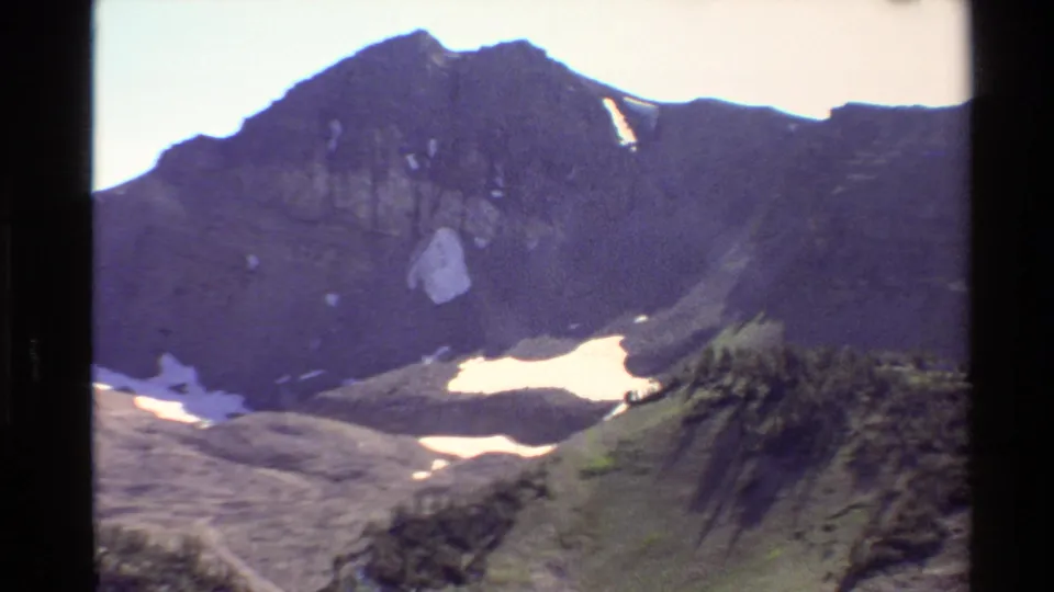 Western USA 1980 8mm frame of a rugged alpine basin with dark peaks, snow patches, rocky slopes, and evergreens.