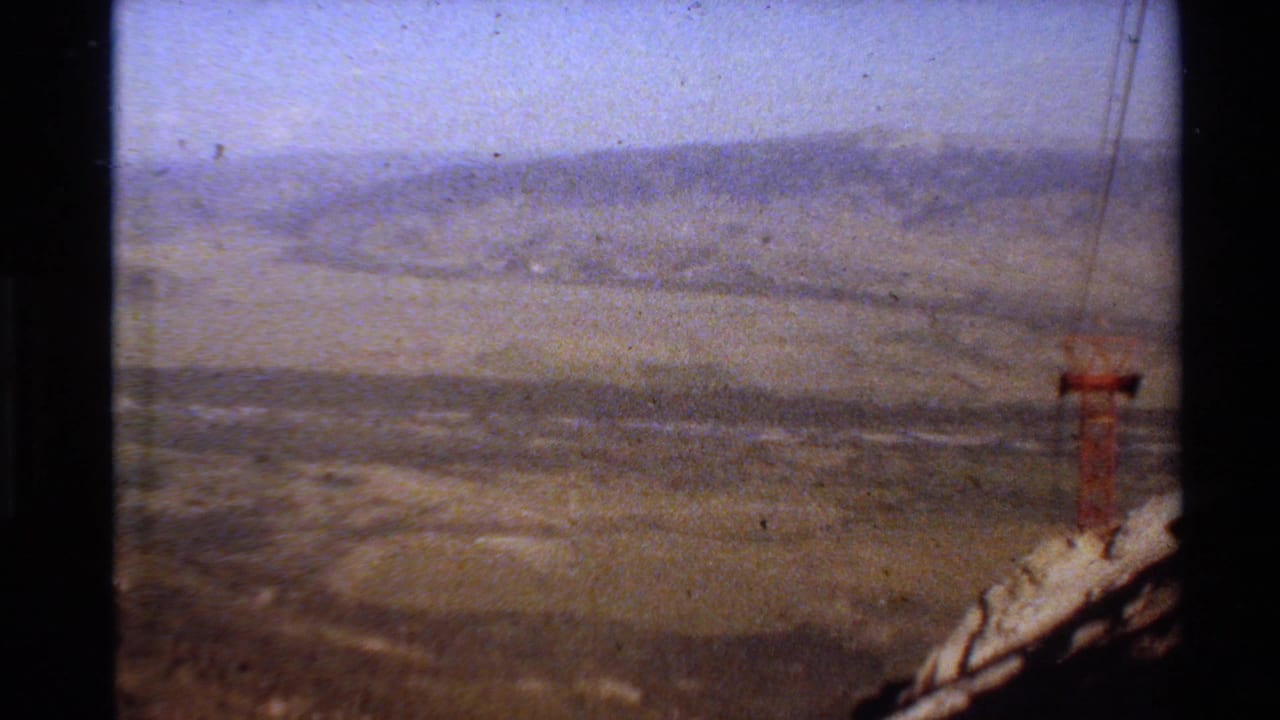1980 Western USA 8mm frame looking across a hazy valley toward distant mountains, with a small tower-like object near the right edge.