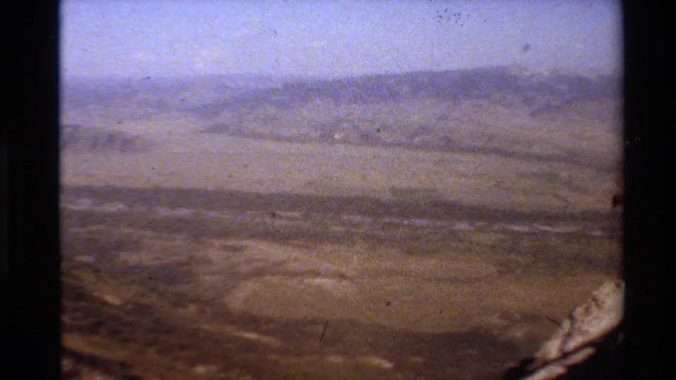 1980 Western USA 8mm frame showing a wide, dry valley and distant mountain ridges from a handheld elevated viewpoint.