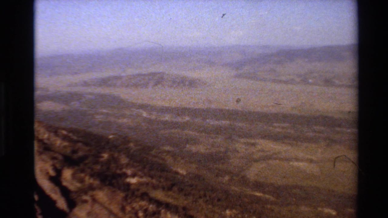 1980 Western USA 8mm frame showing layered brown mountain ridges under a pale hazy sky.