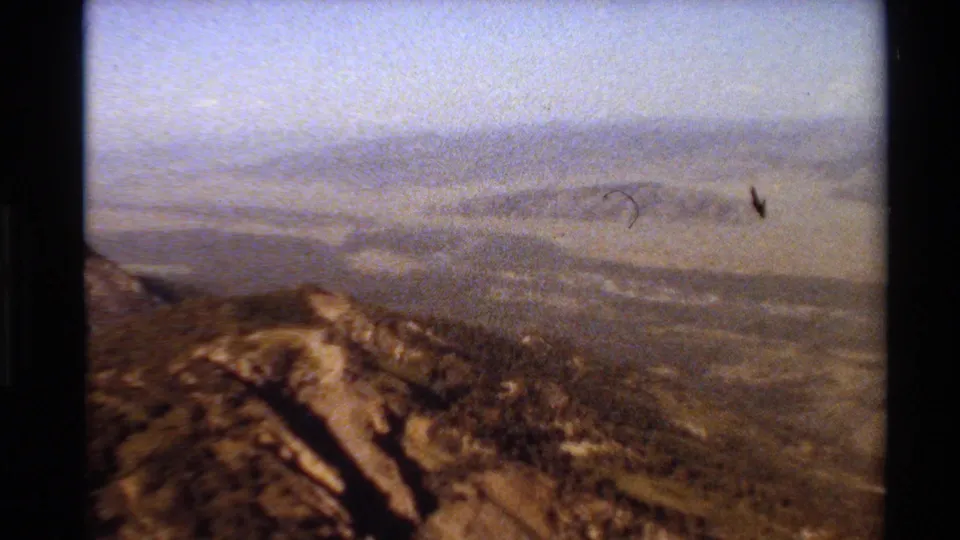 1980 Western USA 8mm frame showing a dry ridgeline against a broad hazy valley and distant hills.