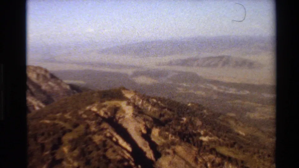 1980 Western USA 8mm frame of a brown mountain ridge overlooking distant valleys beneath a hazy sky.