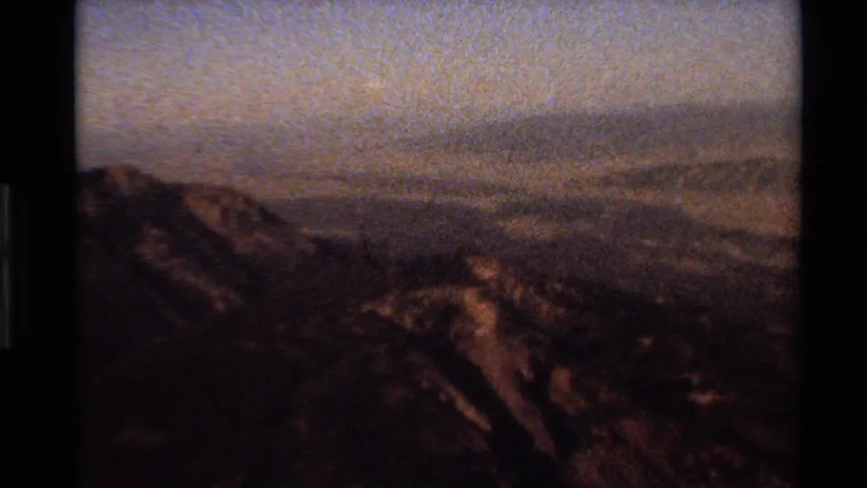 End-of-clip 8mm frame darkens over a Western U.S. mountain panorama, with ridge shapes still visible against a hazy sky.