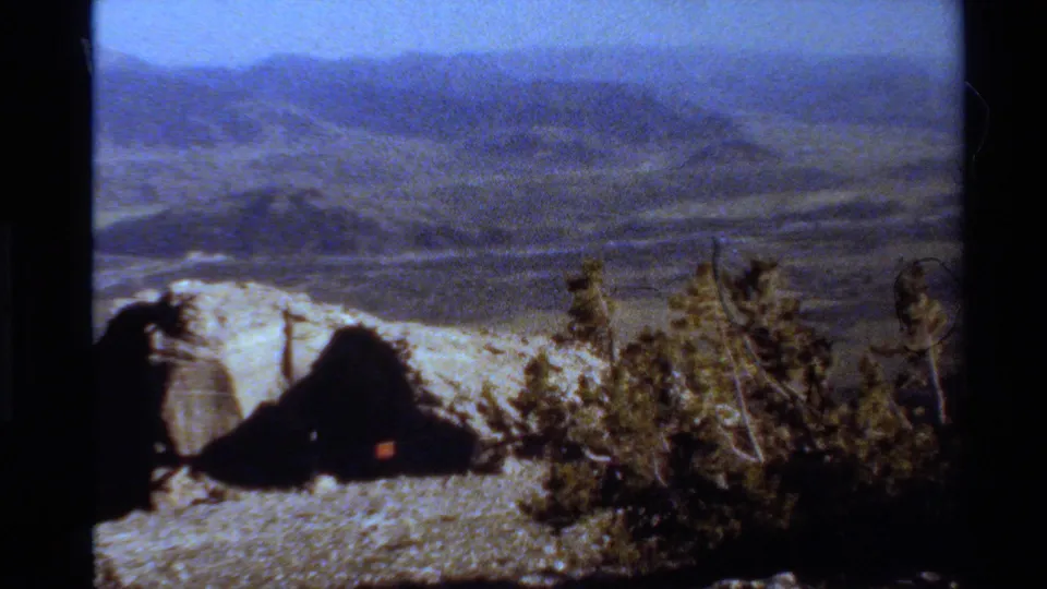 Wide 1980 Western USA 8mm view of hazy mountain ridges, rocky foreground, and sparse evergreen trees.