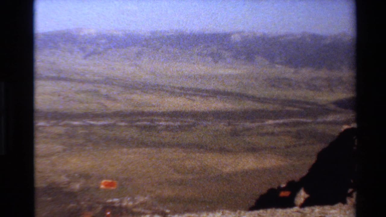 Circa-1980 8mm home-movie frame showing Western U.S. mountain terrain, distant ridgelines, and a dark foreground rock edge.