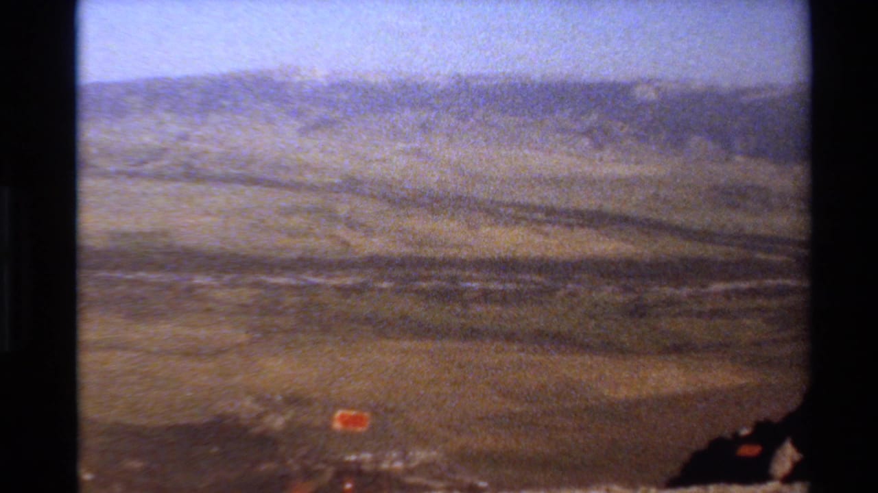 8mm travel footage frame of a hazy Western U.S. mountain panorama with dry terrain and distant ridge lines.