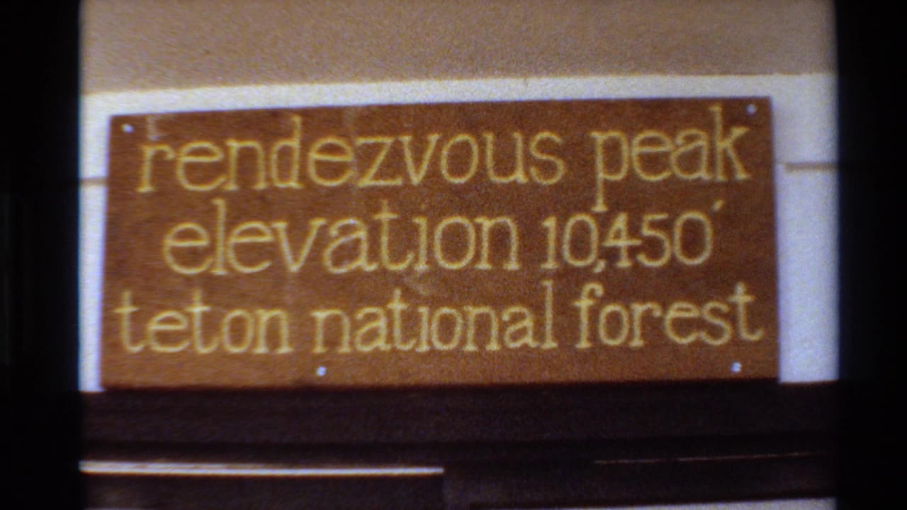 Close 8mm view of the Rendezvous Peak sign, with gold lettering naming Teton National Forest and elevation 10450 feet.