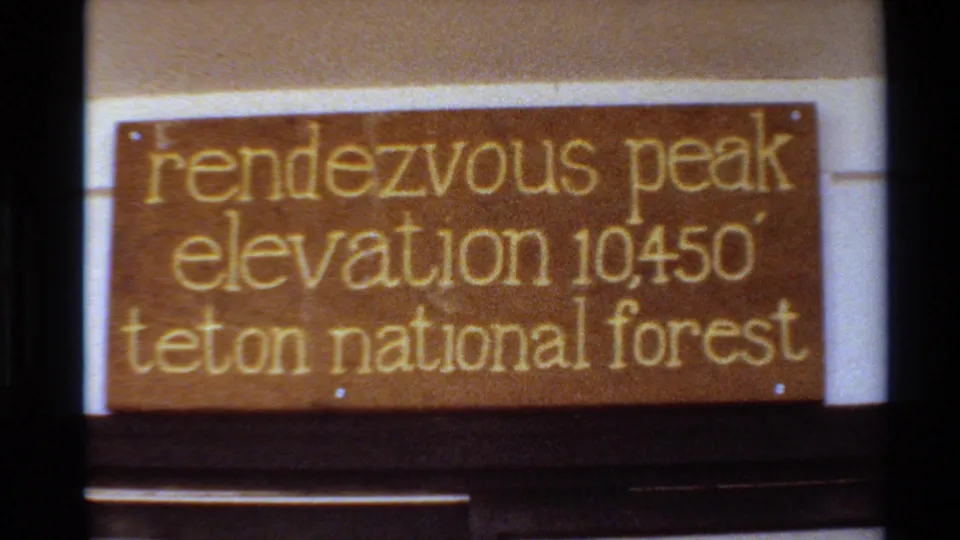 Close 8mm view of the Rendezvous Peak sign, with gold lettering naming Teton National Forest and elevation 10450 feet.