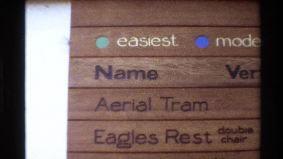 1980s 8mm close-up of a wooden ski-area sign showing colored dots, partial headings, and Eagles Rest double chair text.