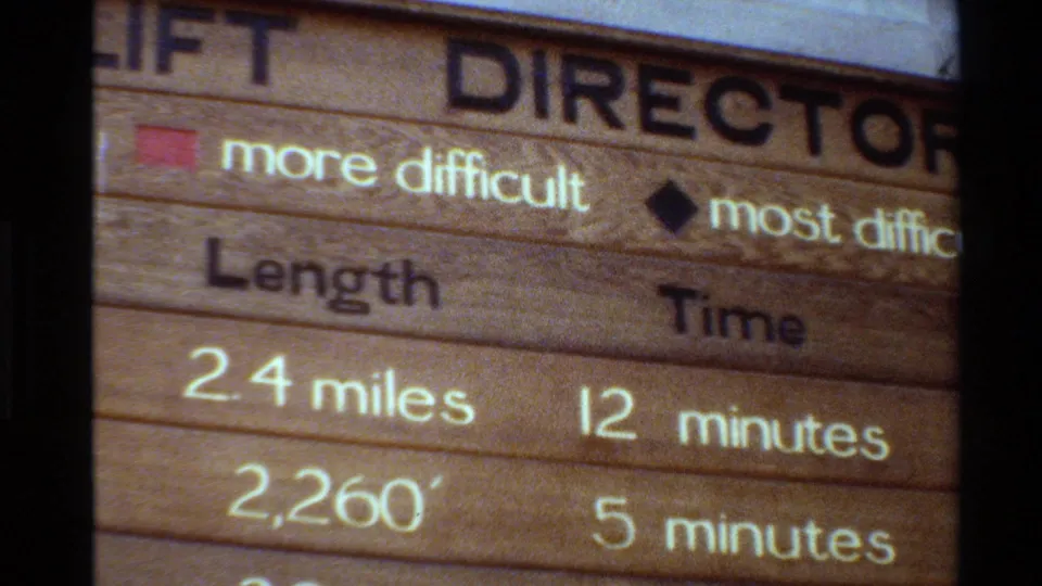The final frame holds on the ski lift direction sign, showing 2.4 miles, 12 minutes, 2,260, 5 minutes, and difficulty symbols on weathered wood.