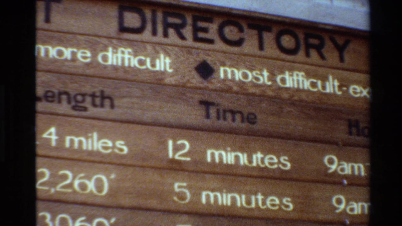 1980 8mm frame showing part of a wooden hiking trail directory with mileage, time, hours, and difficulty information.